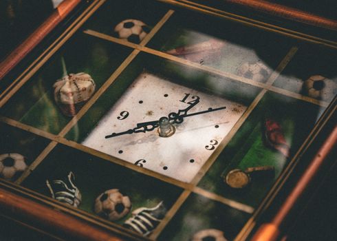 A vintage clock featuring sports-themed decorations like soccer balls and baseballs.