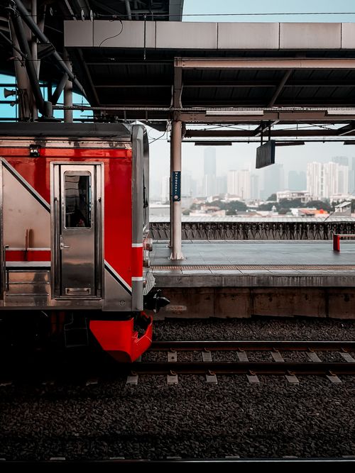 Free A red train at an urban station with city skyline in the background, captured during the day. Stock Photo