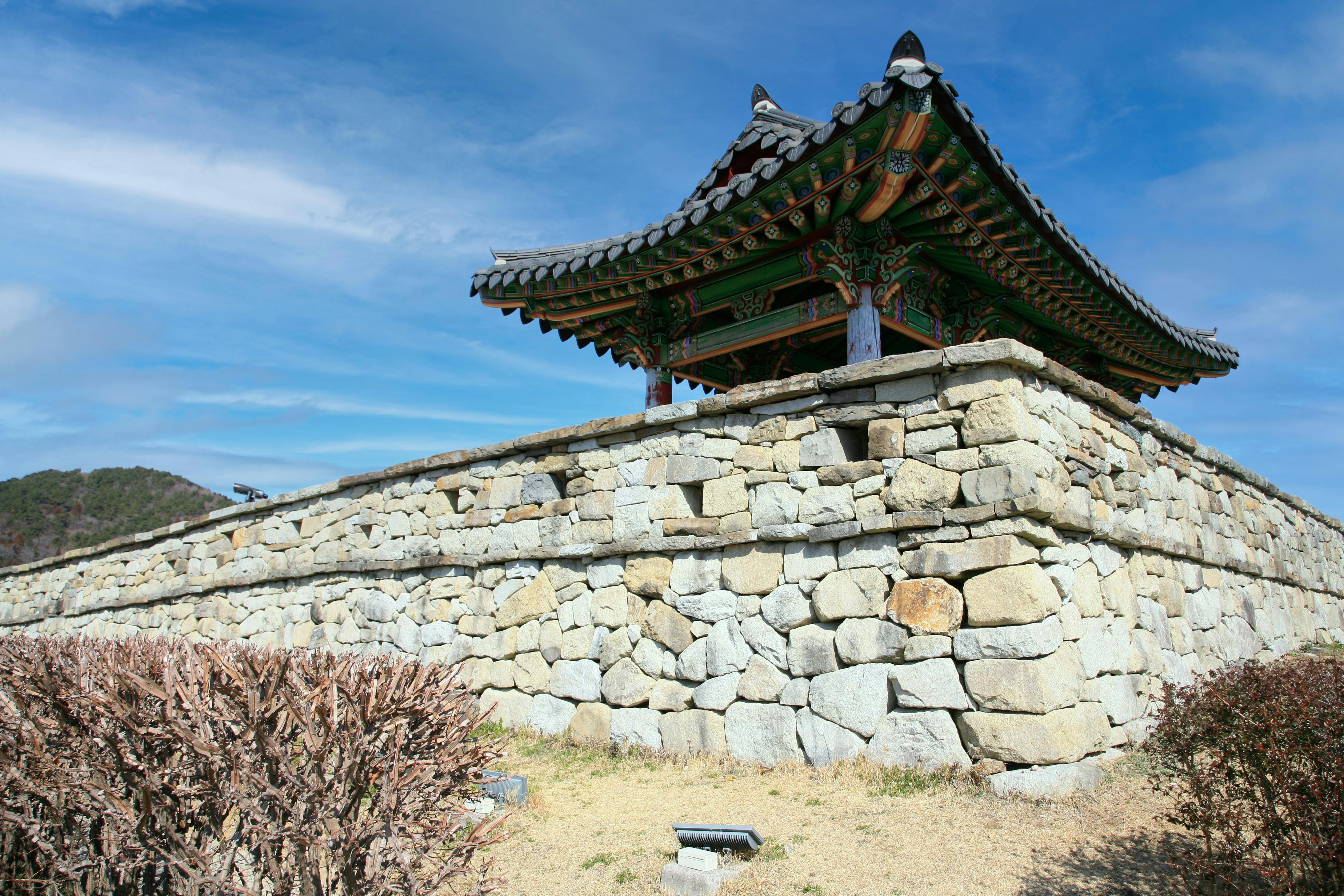 Historic Korean pavilion atop a stone wall against a bright blue sky. Clear day view.