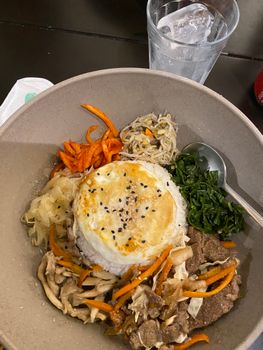 Top view of a vibrant Korean bibimbap dish with a variety of fresh ingredients in a ceramic bowl.