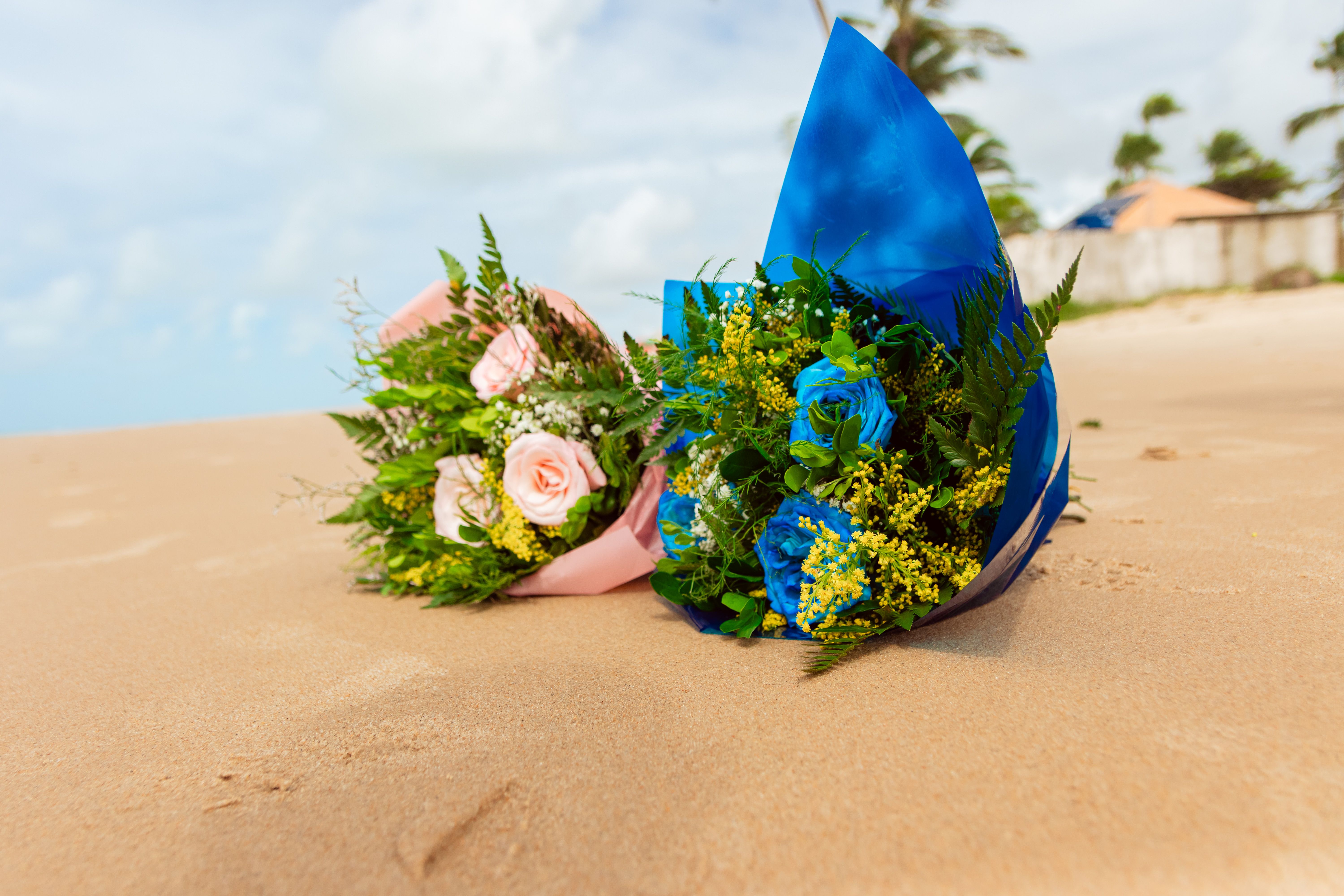 Vibrant blue and pink flower bouquets resting on a tropical sandy beach.