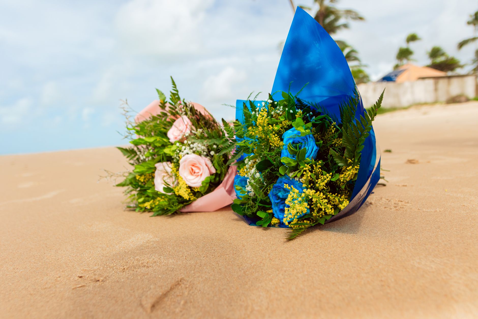Vibrant blue and pink flower bouquets resting on a tropical sandy beach.