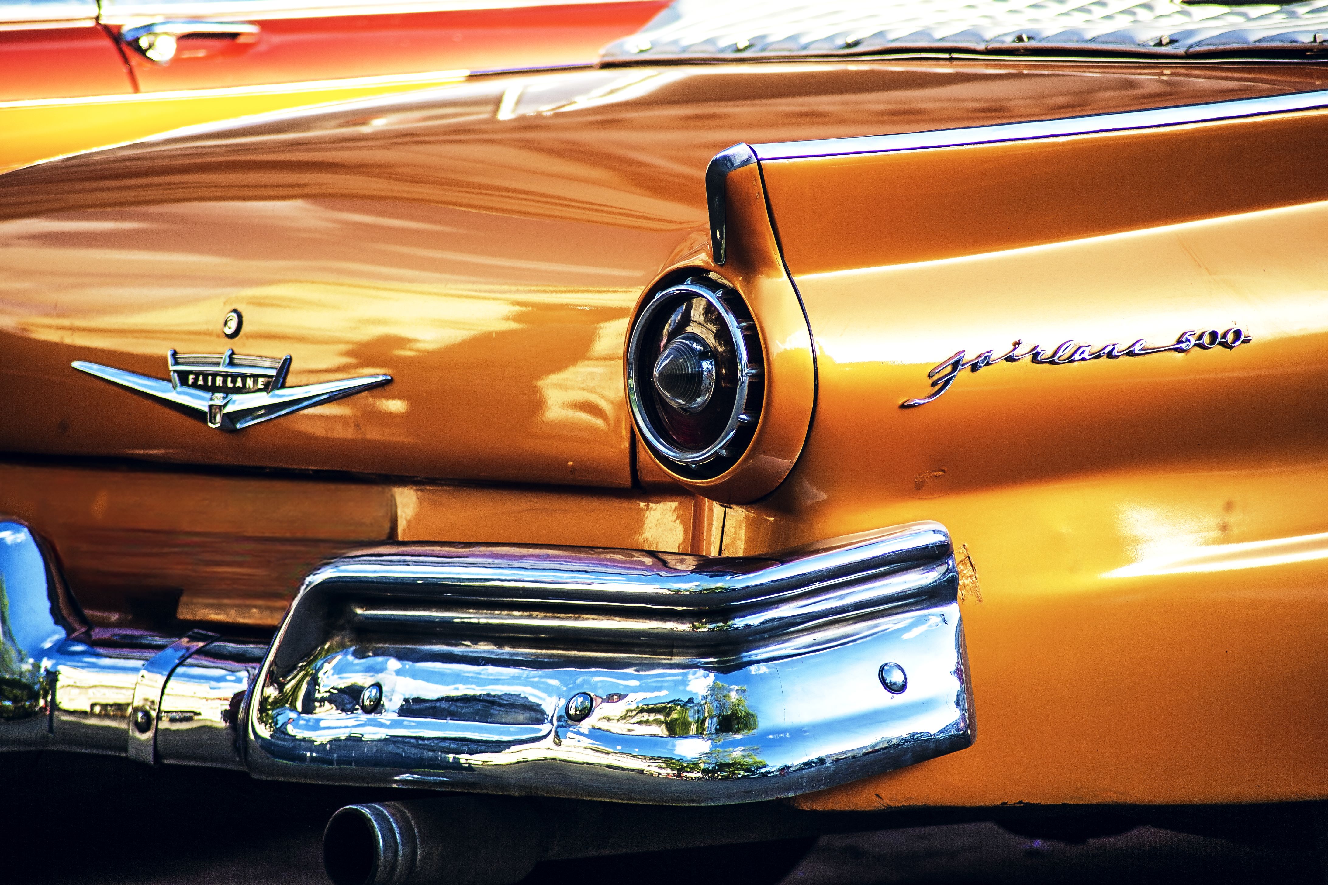 Closeup of a vintage orange Ford Fairlane 500 with chrome details highlighting its classic charm.
