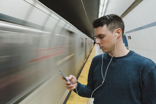 Free A man listening to music on earphones while waiting on a subway platform. Stock Photo