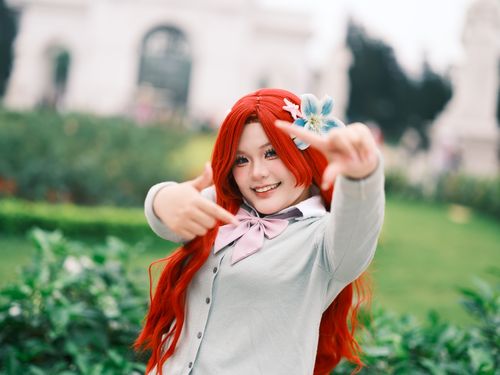 Free Cheerful cosplayer with red hair and floral accessory posing outdoors in a garden, Hanoi, Vietnam. Stock Photo
