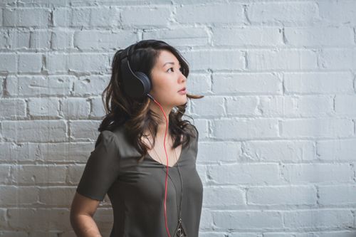 Free Young woman with headphones looking thoughtful against a white brick wall. Stock Photo