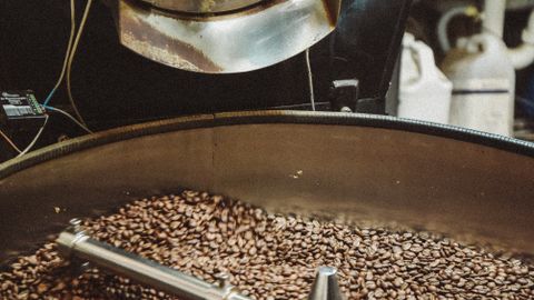 A detailed view of an industrial coffee roaster processing fresh coffee beans, highlighting the machinery and rich texture.