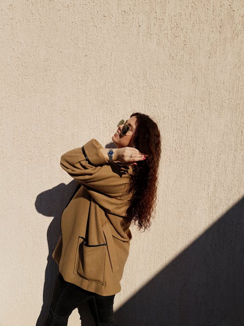 Woman in Brown Coat Near Concrete Wall