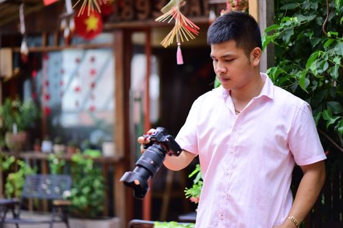 Free Man in a pink shirt holding a camera in a vibrant outdoor cafe setting. Stock Photo