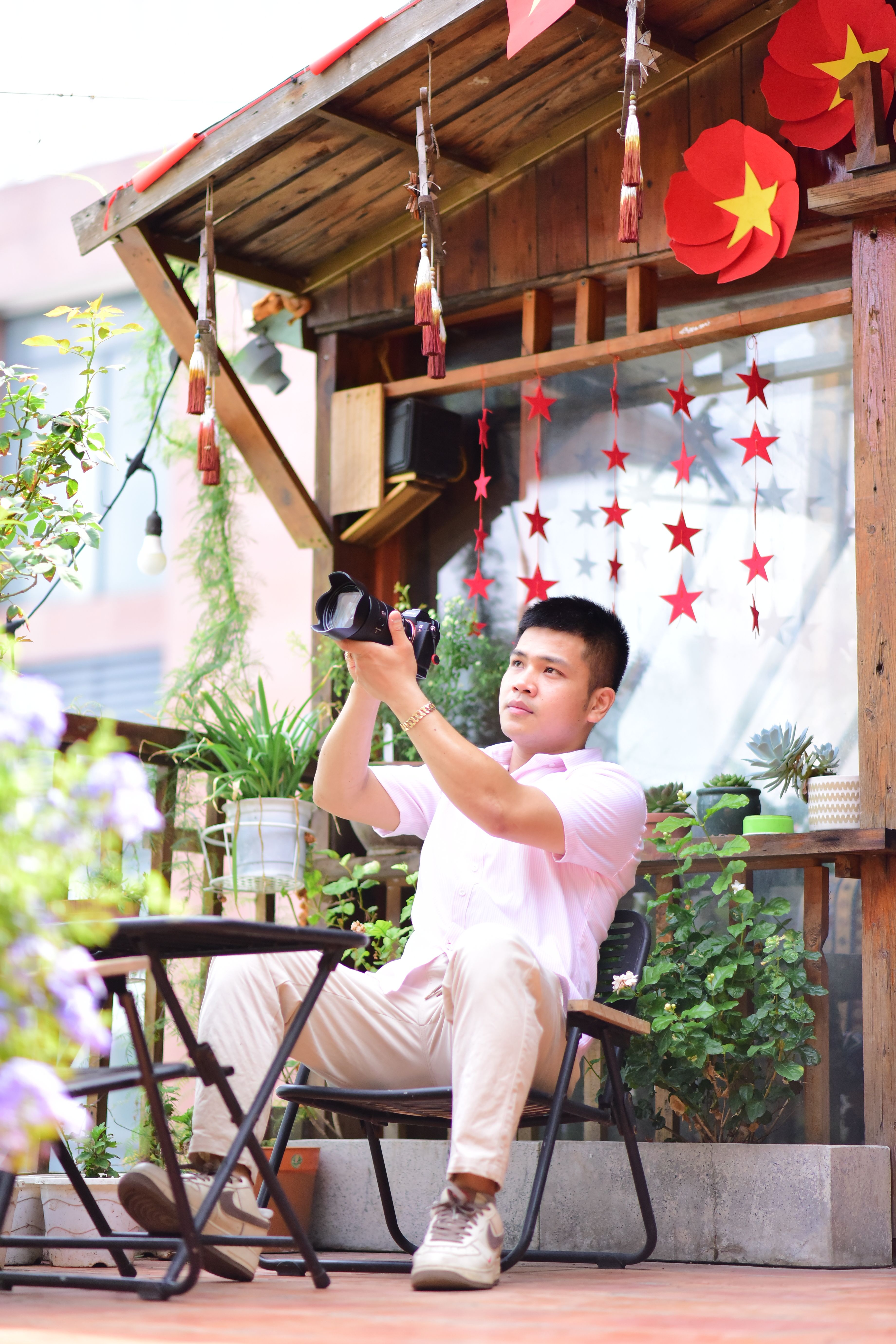A young man takes photos on a cozy patio adorned with red decorations and greenery.