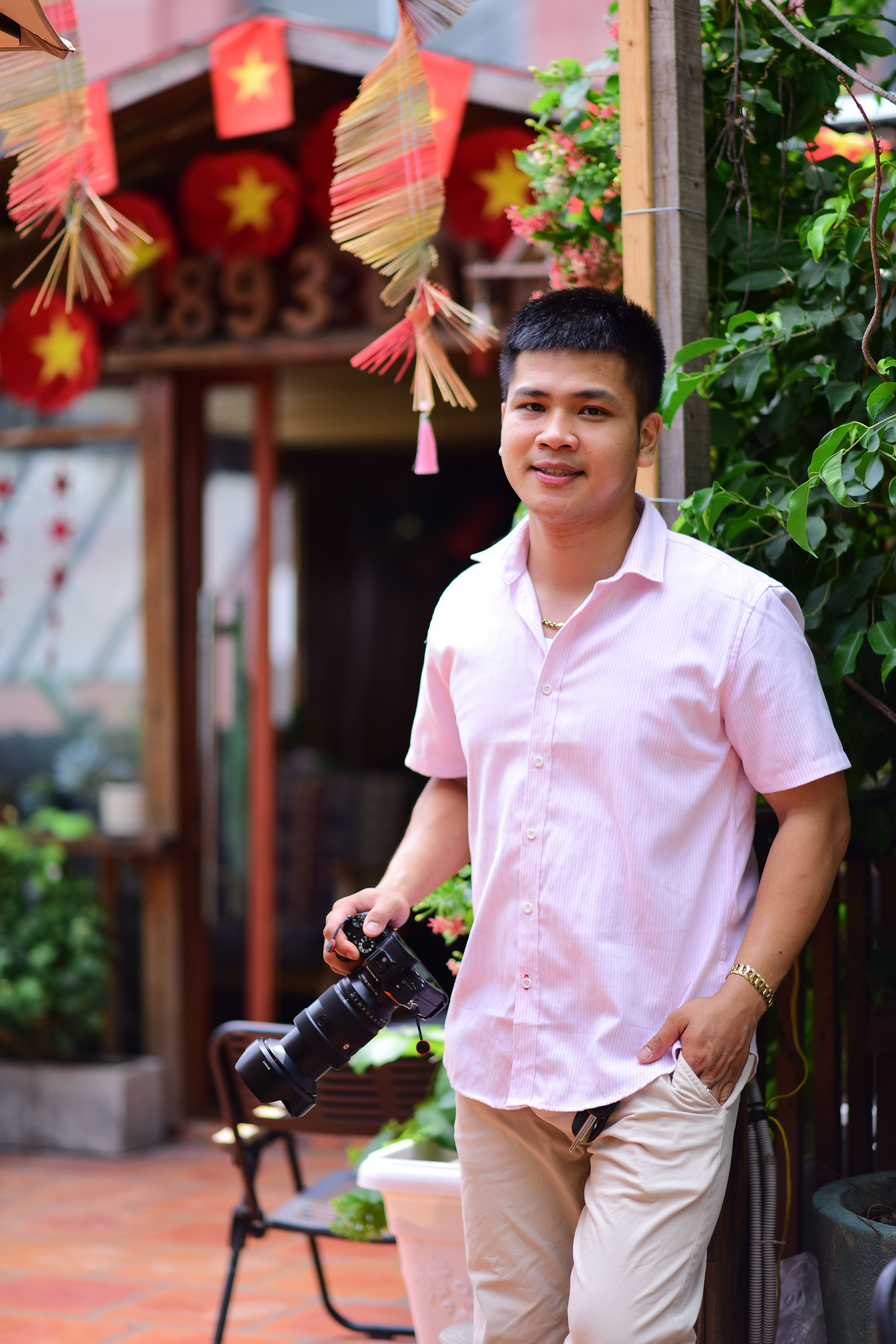Smiling photographer holding camera outdoors with festive decor background.
