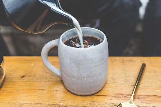 A cozy scene of milk being poured into a coffee mug on a wooden table.