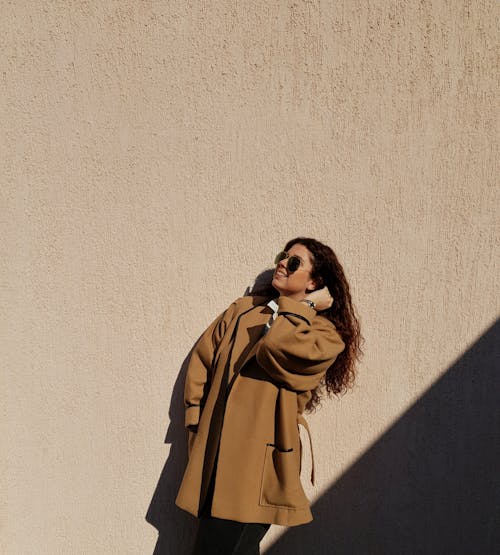 Woman in Brown Coat Standing Beside Brown Wall