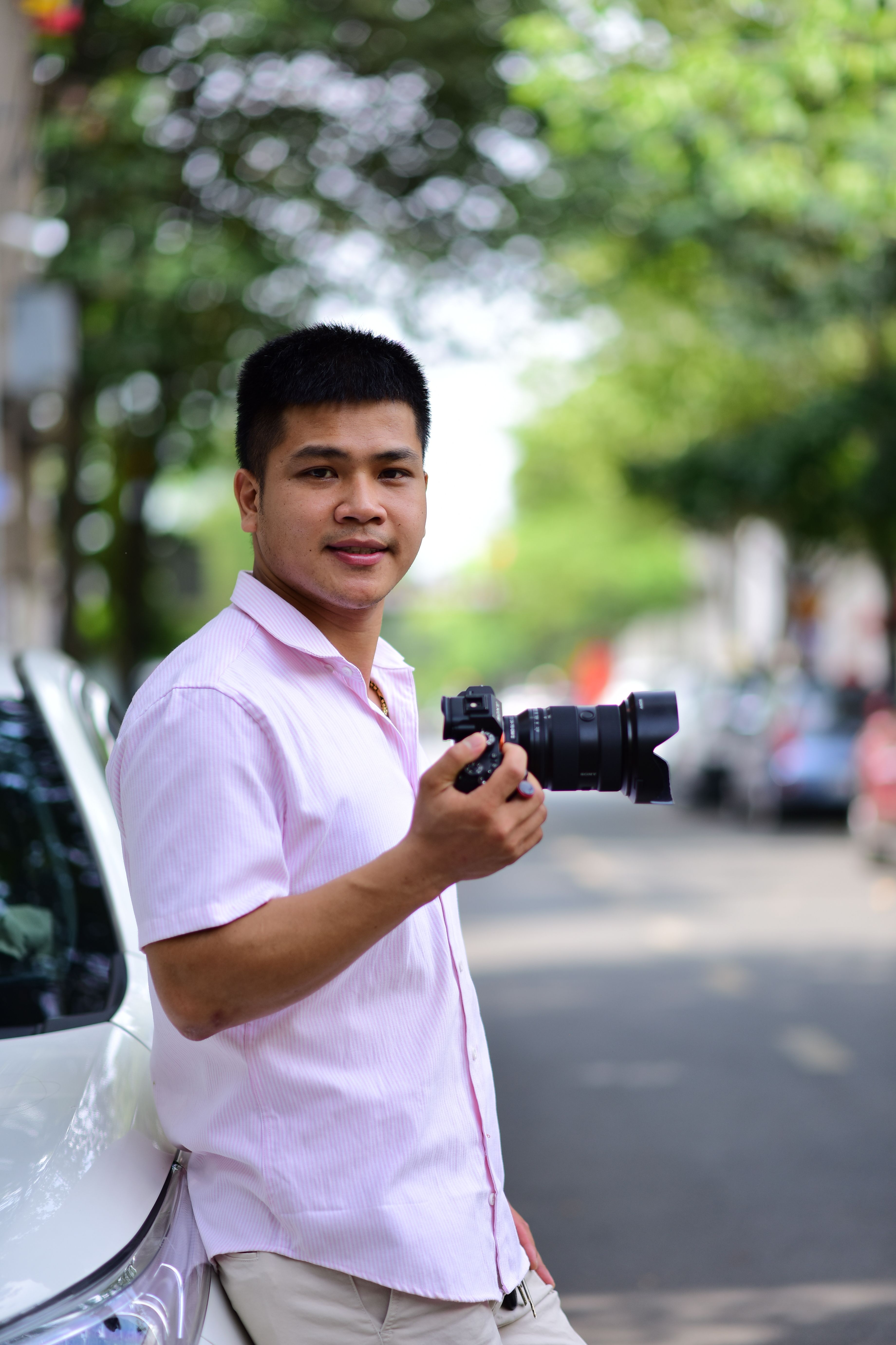 Casual portrait of a male photographer holding a camera on a sunny urban street.