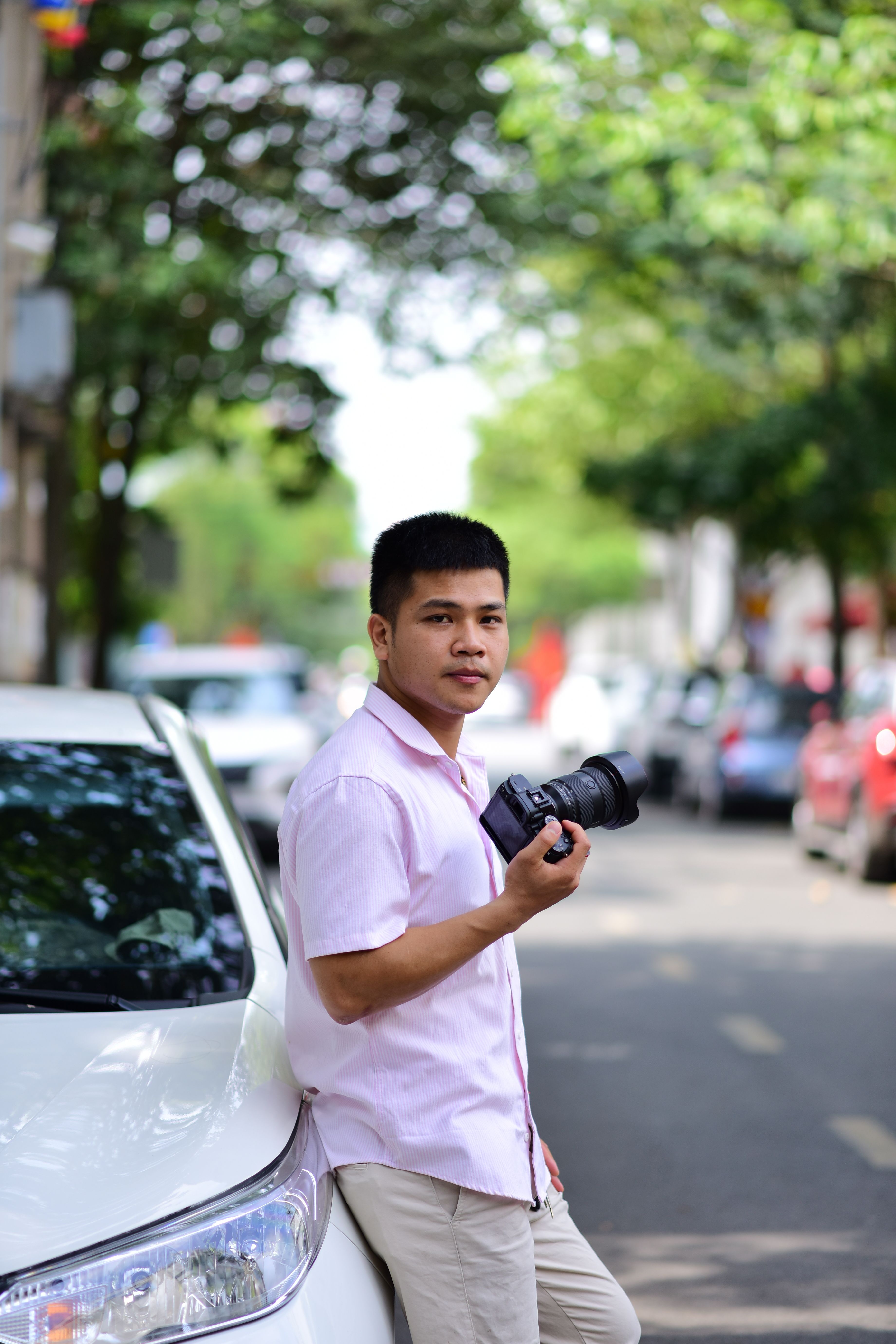 Young male photographer stands casually with camera on urban street during the day.