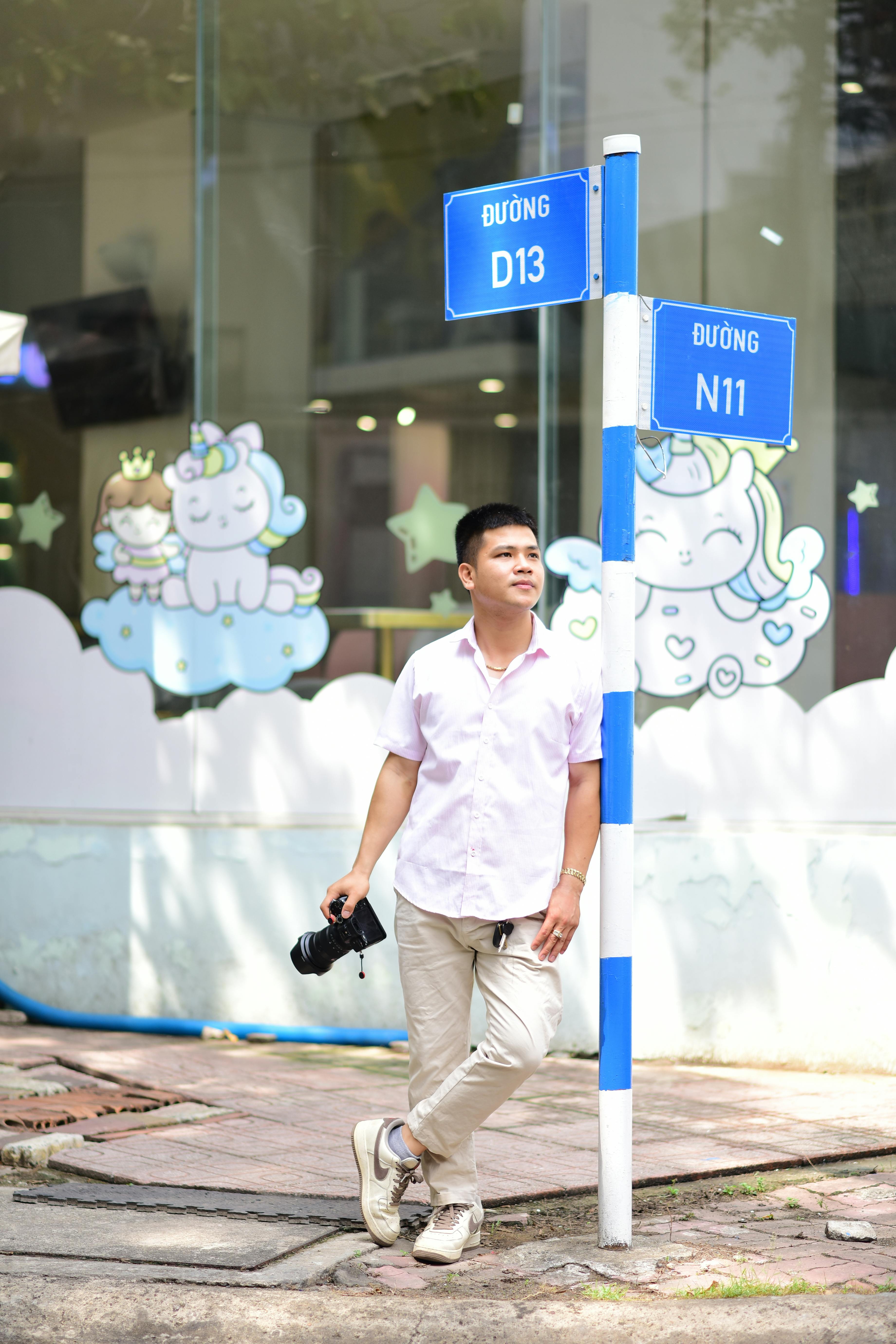 Man with camera leans on street signs near playful window display under bright daylight.