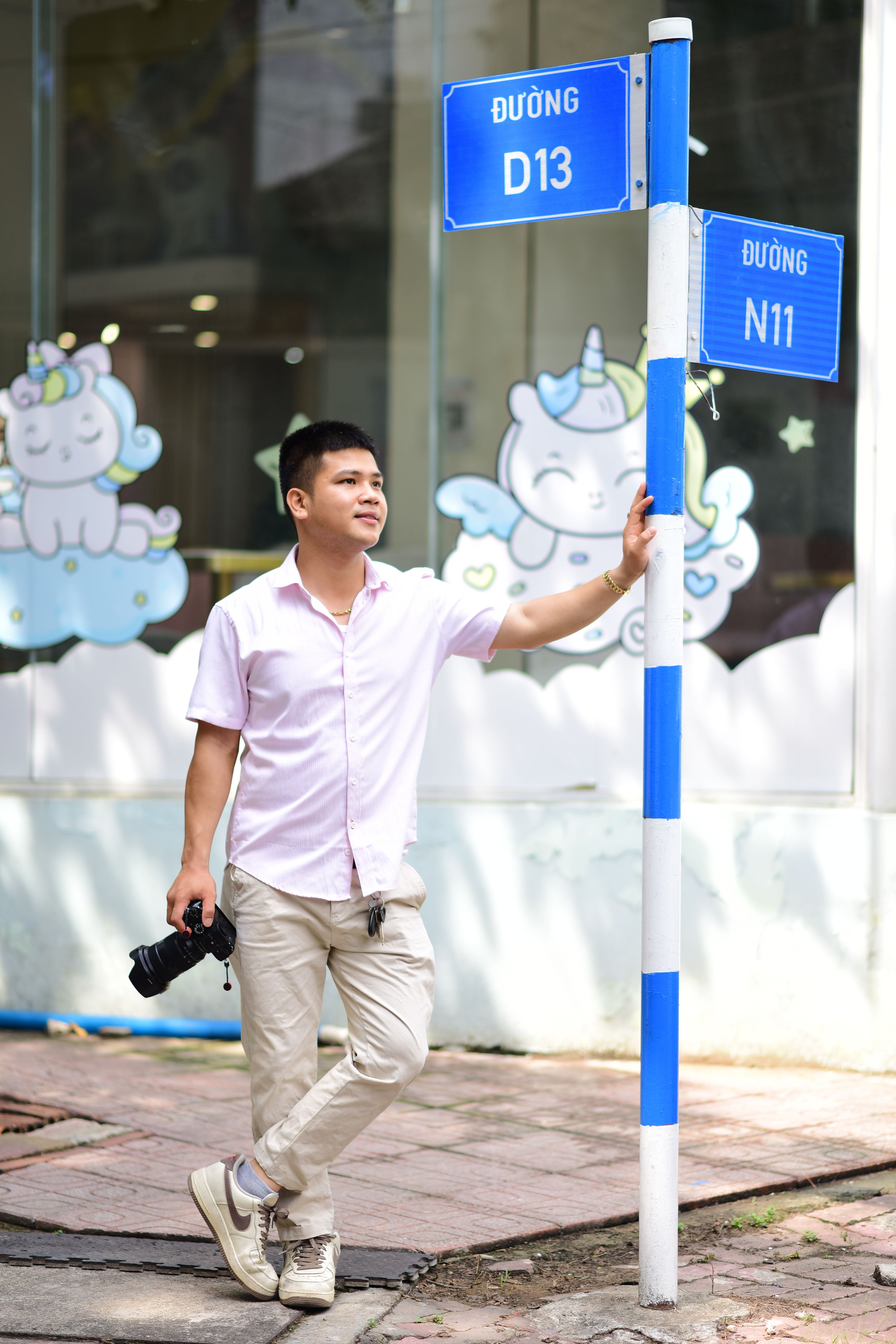 Casual young man with camera standing by street sign in urban setting.