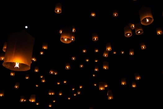Sky lanterns float against a dark night sky during a traditional festival in Thailand.