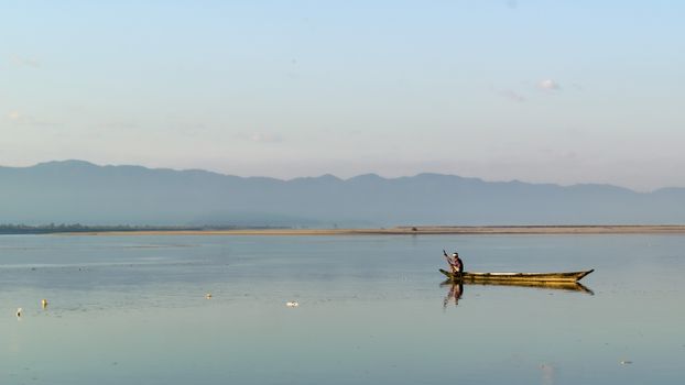 A serene view of a fisherman in a boat on the calm Brahmaputra River near Biswanath Charali, Assam.