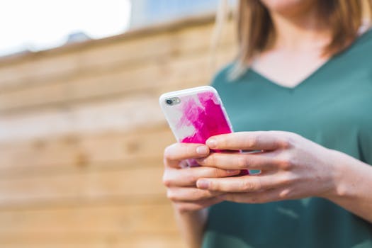 Woman using a smartphone with a colorful case outside on a sunny day.