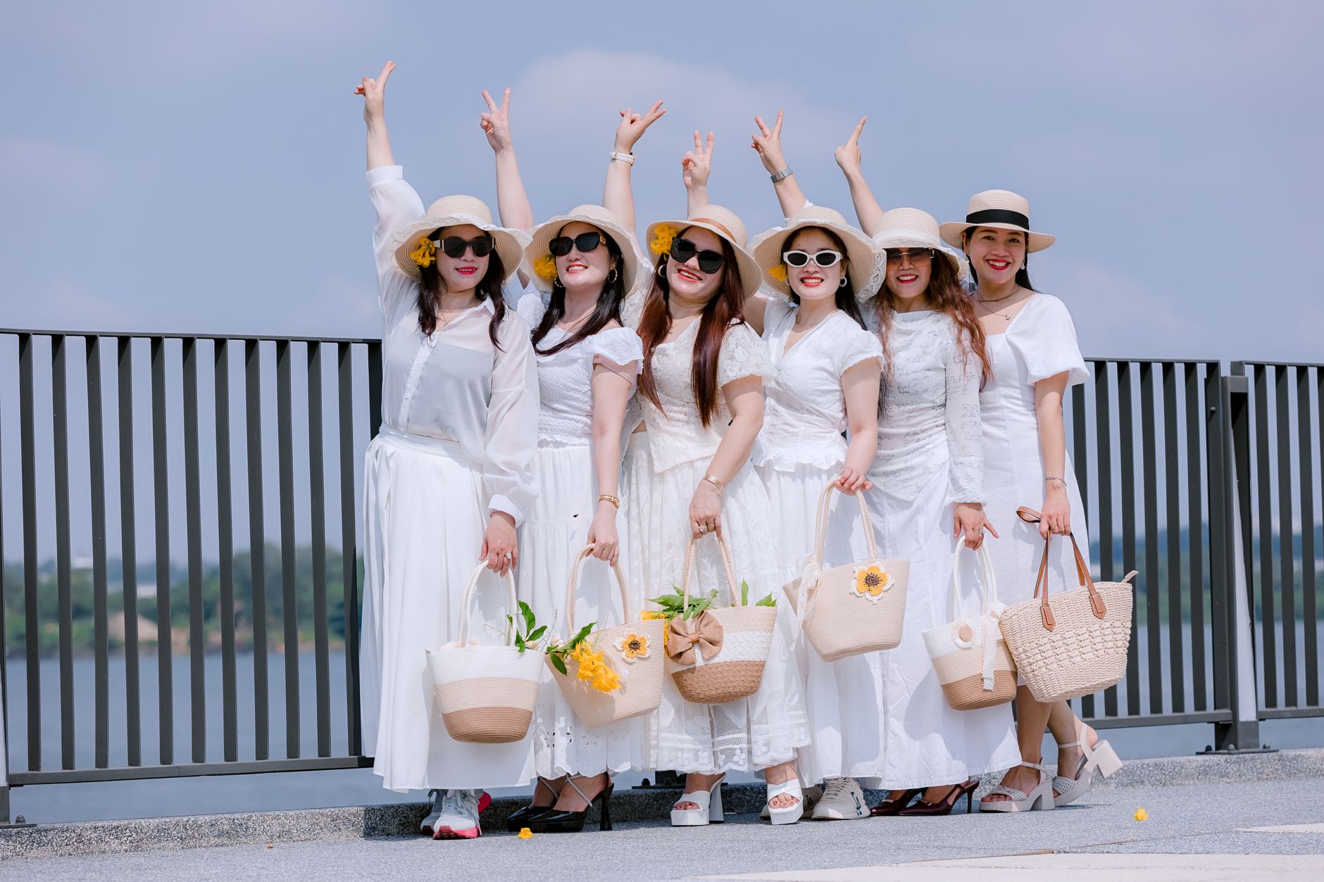 A joyful group of women in white dresses and hats pose cheerfully outdoors.