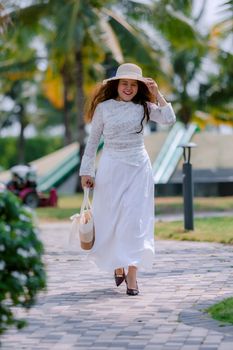 Cheerful woman in white dress and hat walking outdoors on a bright day.