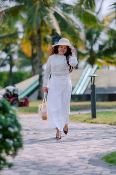 Happy woman in white dress and hat walking on a sunny day in a park setting.
