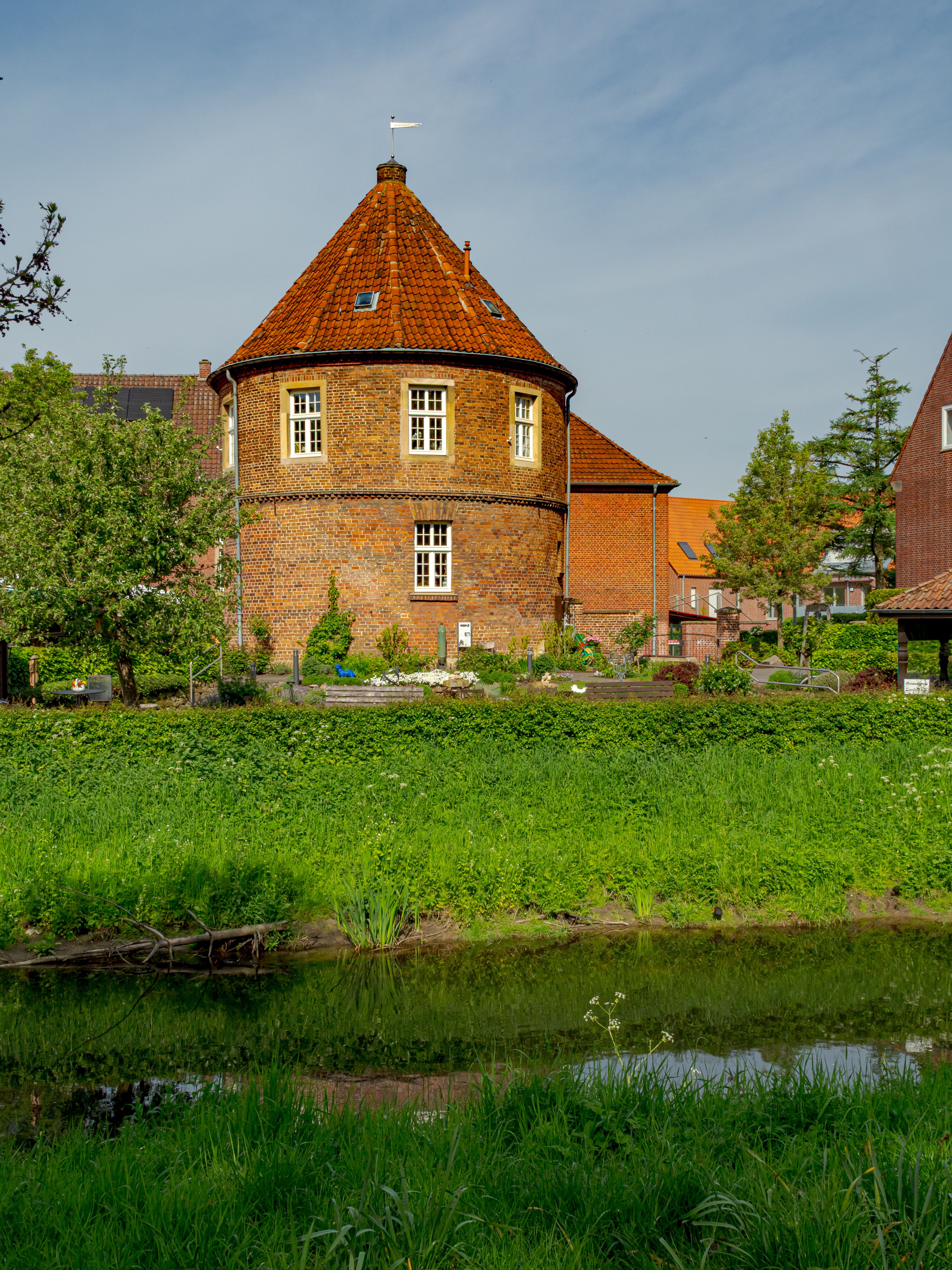 Charming historic brick tower with red roof by a serene canal in Coesfeld, Germany.