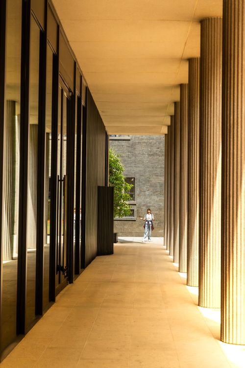 Free A person walking through a sunlit corridor of modern architecture with columns. Stock Photo