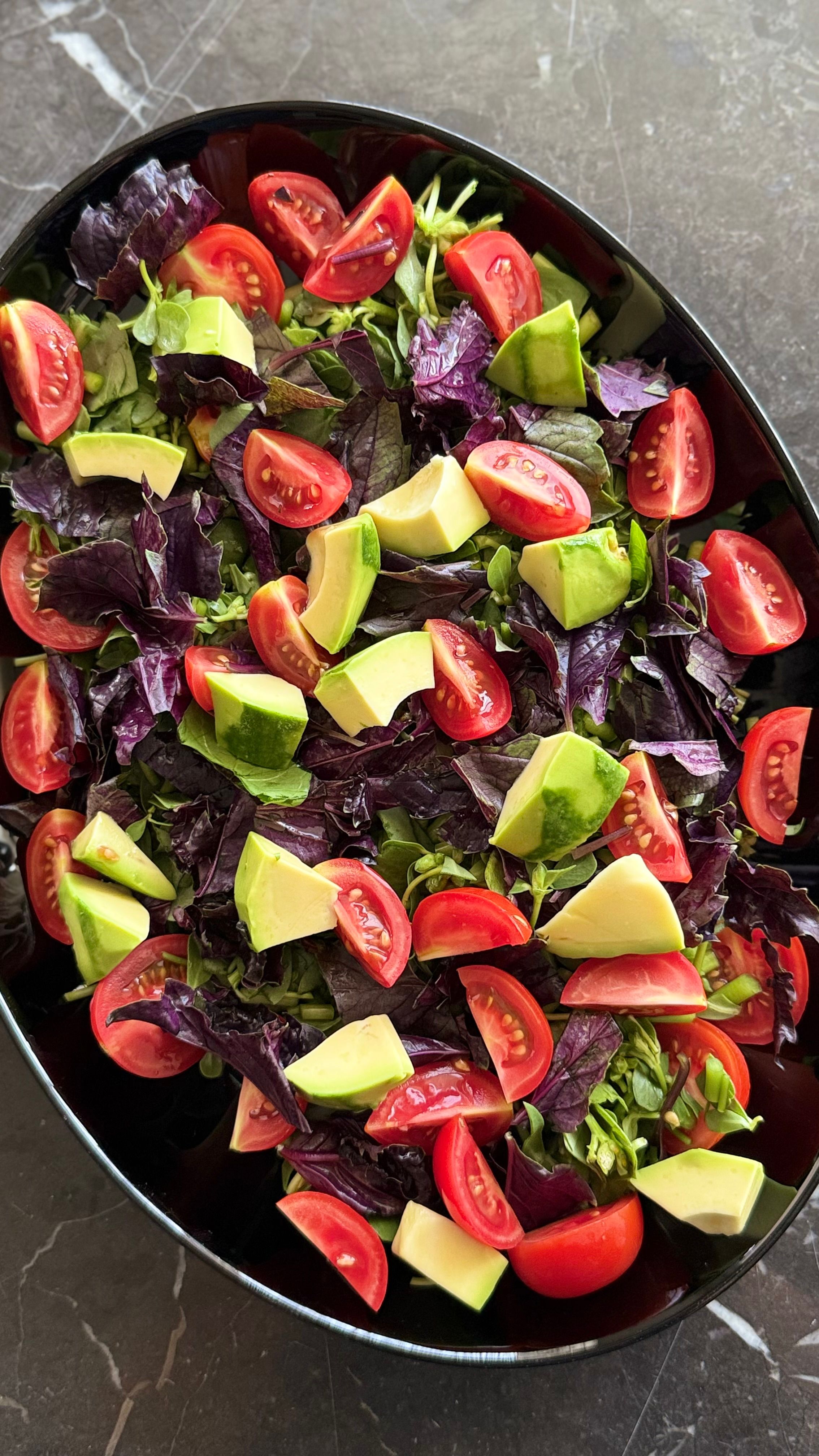 Vibrant salad with tomatoes, avocado, and greens on a dark marble surface.