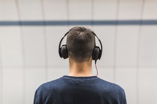 Binaural beats: czym są i jak wpływają na świadomość? – Najczęściej zadawane pytania 1 Back view of a man listening to music with headphones indoors.