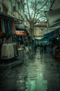 Moody street scene capturing rainy reflections in a lively urban market alley.