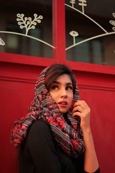 A beautiful woman wearing a colorful headscarf poses elegantly against a red backdrop.