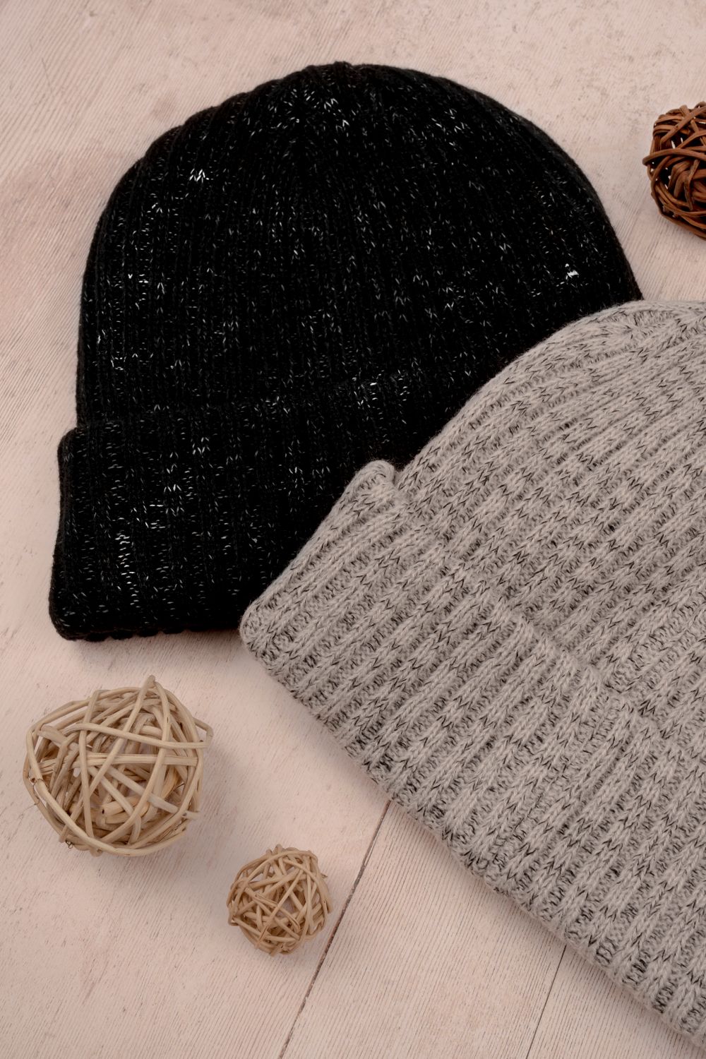A structured cap and a knitted beanie with small embroidered marks, next to a grey felt sauna hat, on a slate grey surface