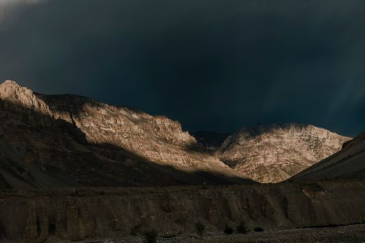 Dark clouds cast shadows over rugged mountains in Spiti Valley.