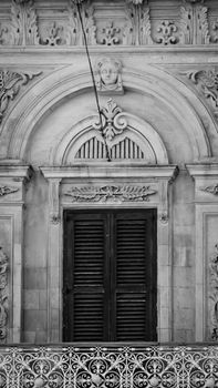Black and white image of an ornate vintage architectural facade featuring intricate carvings and shuttered windows.