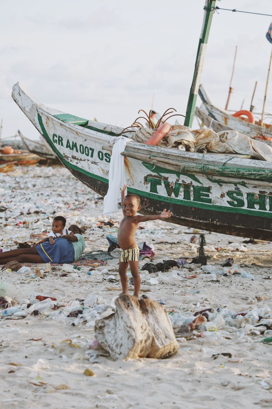 Kinderen spelen in de buurt van vissersboten te midden van plastic afval op het strand van Accra in Ghana, wat de aandacht vestigt op milieuproblemen.