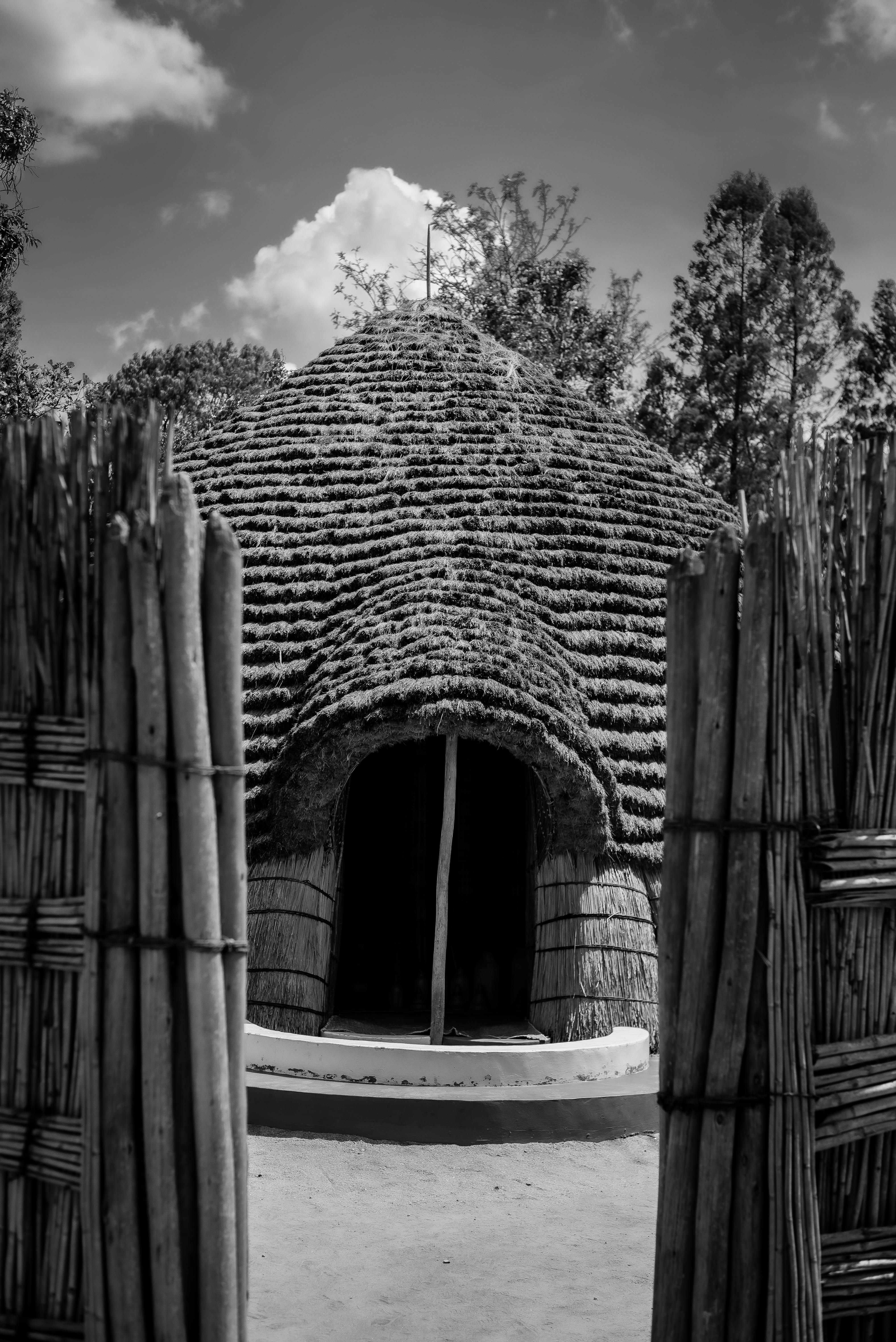 A traditional thatched Rwandan hut seen through an open bamboo gate, showcasing African architectural style.