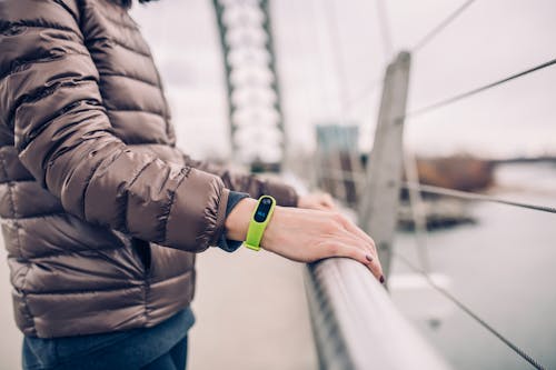 Selective Focus Photography of Man in Bubble Jacket Wearing Xiaomi Mi Band 2 Fitness Band While Holding Bridge Rails
