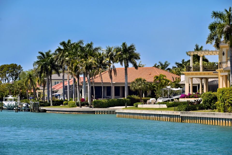 Tile-roofed waterfront homes and palm trees along a seawall