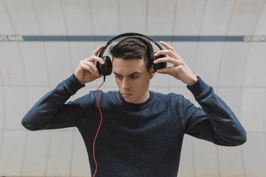 A young man adjusting headphones indoors, focused and fashionably dressed.