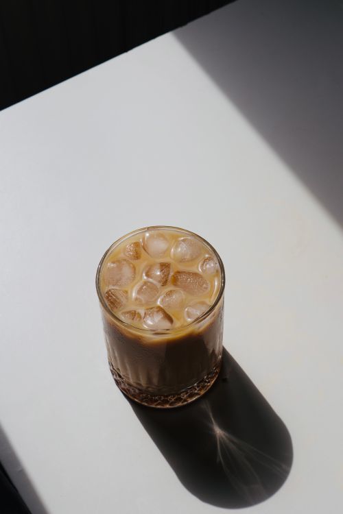 Free A glass of iced coffee with ice cubes placed on a bright, minimalist surface with dramatic lighting. Stock Photo