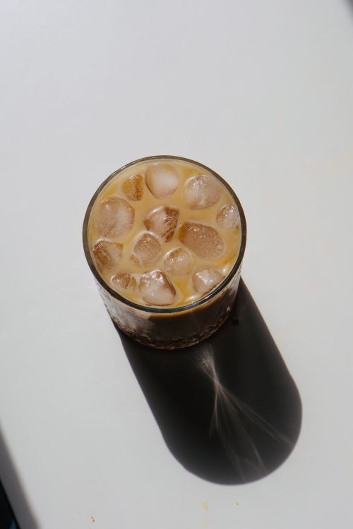 Glass of iced coffee casting a long shadow on a white surface — photo by azra melek on Pexels