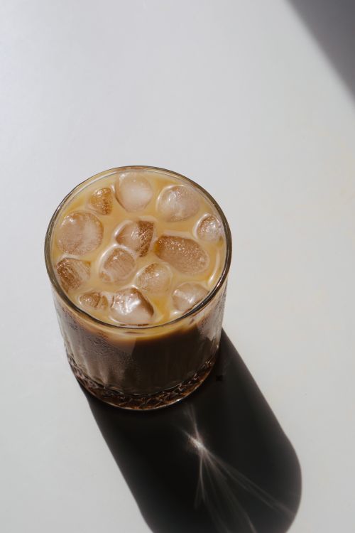 Free A glass of iced coffee with ice cubes casting a shadow on a white surface. Stock Photo
