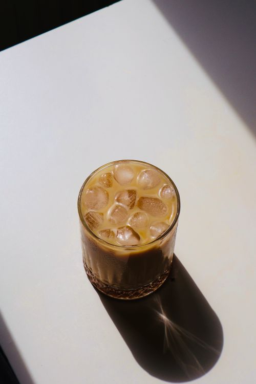 Free A refreshing iced coffee with milk served in a glass on a sunlit table casting a shadow. Stock Photo