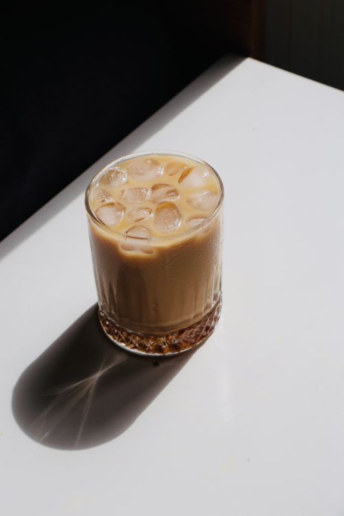Free A glass of iced coffee with ice cubes on a sunny table casting a shadow. Stock Photo