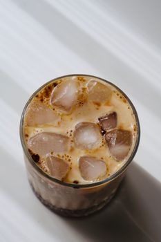 Top view of a refreshing glass of iced coffee with milk and ice cubes, casting soft shadows.