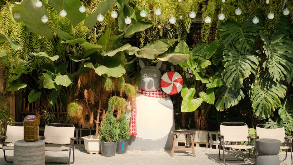 Whimsical outdoor garden scene with lush greenery and a cartoon figure sculpture.