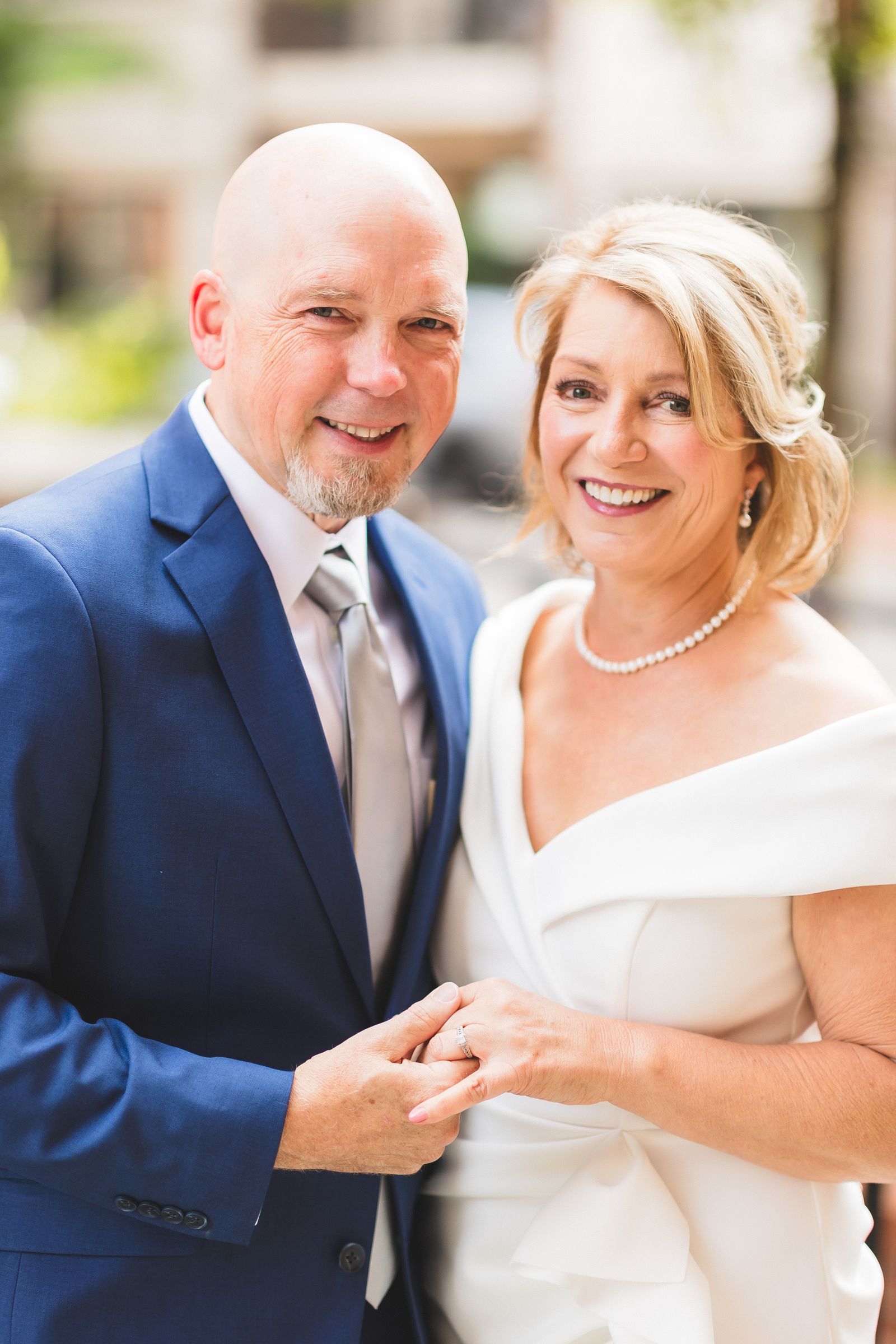 A mature couple in elegant wedding attire poses together outdoors