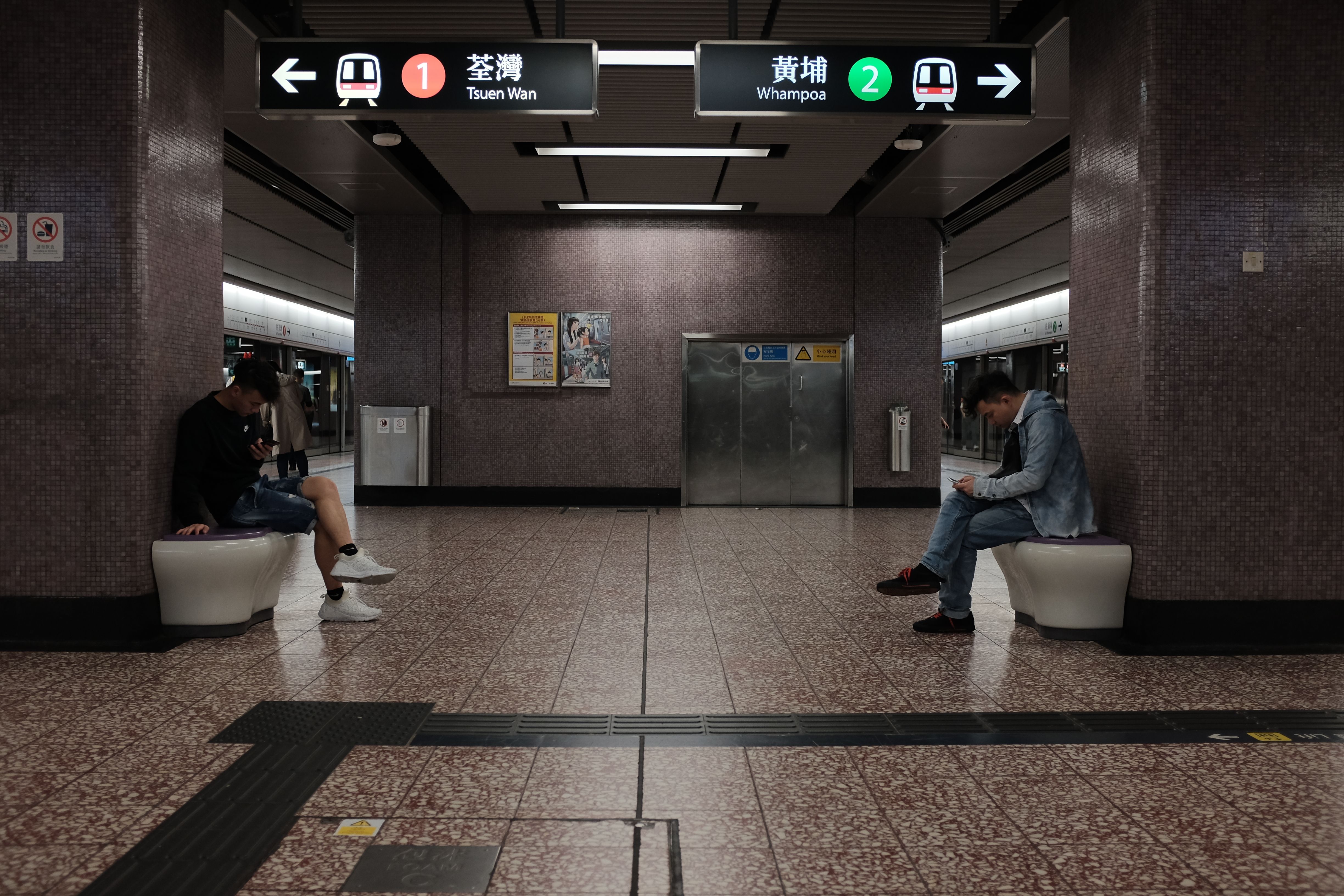 Two men sitting quietly in a Hong Kong subway station, absorbed in their mobile phones.